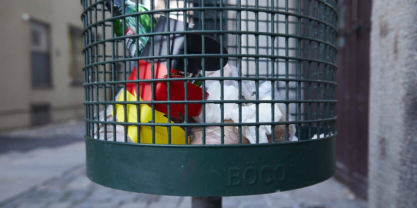 Ein kaputter schwarz-rot-goldener Plastikbecher in einem Mülleimer