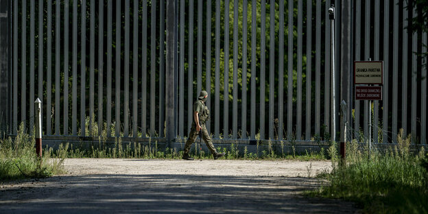 Ein Soldat patrouilliert an einem hohen Metallzaun entlang