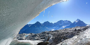 Das Eis des Gletschers schmilz, Wassertropfen fallen, im Hintergrund ein Bergpanorama, die Sonne scheint