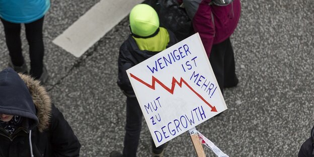 Menschen demonstrieren, einer trägt ein SChild mit einer Wirtschaftskurve, die nach unten weist