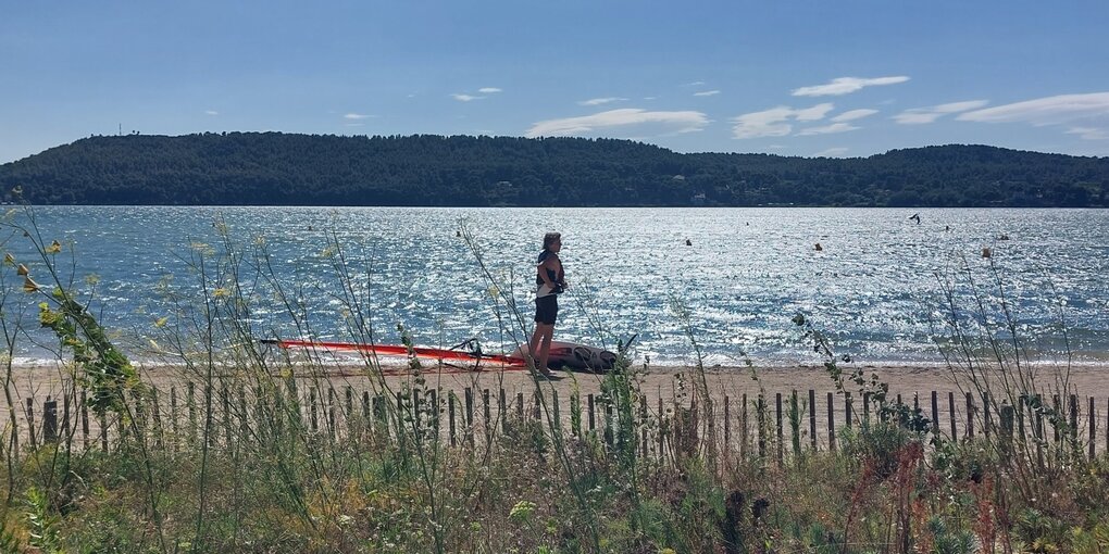 Ein Mann am Meer. Neben ihm liegt ein Windsurf-Board.