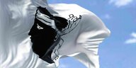 Die korsiche Flagge, eine schwarze Figur auf weißem Hintergrund, weht vor einem blauen Himmel