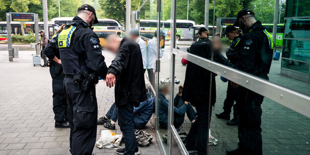 Ein Polizist und eine Polizistin am Hamburger Hauptbahnhof kontrollieren zwei augenscheinlich wohnungslose Männer.