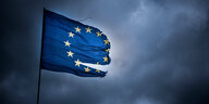 Eine EU-Flagge mit Rissen weht. Im Hintergrund sind dunkle, graue Wolken.