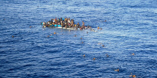 Ein Boot mit Flüchtlingen sinkt im Mittelmeer, einige schwimmen bereits um ihr Leben. Aufnahme von einem Frachtschiff von April 2015.