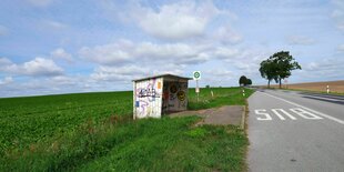 Sommerstimmung, mit Schäfchenwolken. Eine leere Bushaltestelle steht an einer nicht befahrenen Landstraße