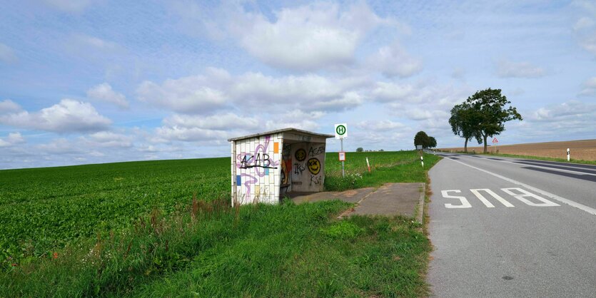 Sommerstimmung, mit Schäfchenwolken. Eine leere Bushaltestelle steht an einer nicht befahrenen Landstraße