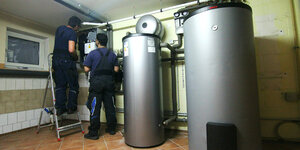 Zwei Handwerker stellen eine gerade installierte Wärmepumpe im Keller einer Doppelhaushälfte ein.
