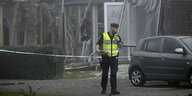 Polizist in Warnweste vor einem schwer beschädigten Haus, in dem eine Bombe explodierte und dabei eine Frau getötet wurde
