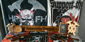 Waffen und rechtsextremistische Devotionalien liegen auf einem Tisch, darunter Straßenschilder mit "Adolf-Hitler-Platz" und Plakate zur Waffen-SS