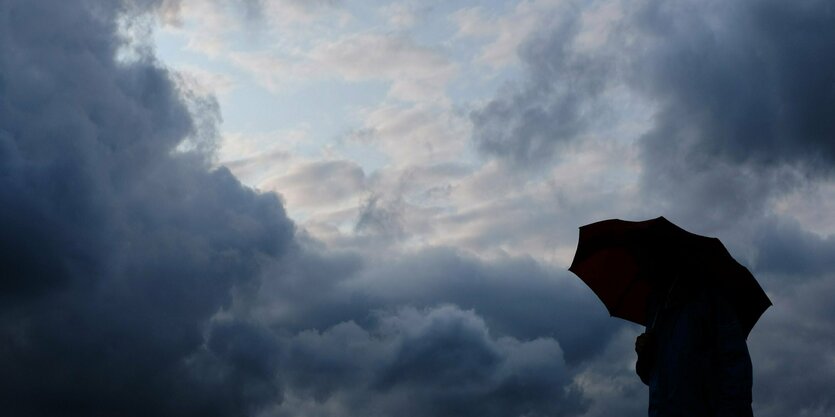 Ein Mann geht mit einem Regenschirm vor aufziehenden dunklen Wolken spazieren.