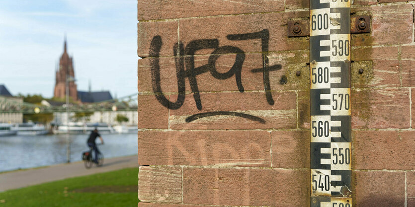 Eine Wasserpegelmarkierung ist an einer Mauer direkt am Mainufer angebracht