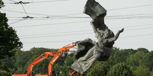 Bagger stürzen eine große stilisierte Frauenfigur aus Beton