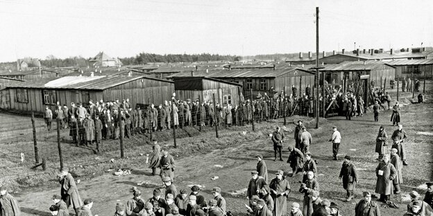 Historische Aufnahme von Männern, die ein Lager mit Holzlatten auf der Schulter verlassen