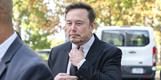 Elon Musk im Anzug, der sich seine Krawatte zurechtzieht