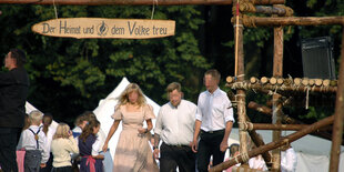 Eine Gruppe Kinder und drei Erwachsene stehen vor weißen Stoffzelten und unter einem Holzschild auf dem "Der Heimat und dem Volke treu" steht