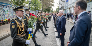 Ukraines Außenminister Kuleba empfängt am Mahnmal für Kriegopfer in Kiew seine EU-Amtskollegen, die jeweils von Soldaten Blumen überreicht bekommen.