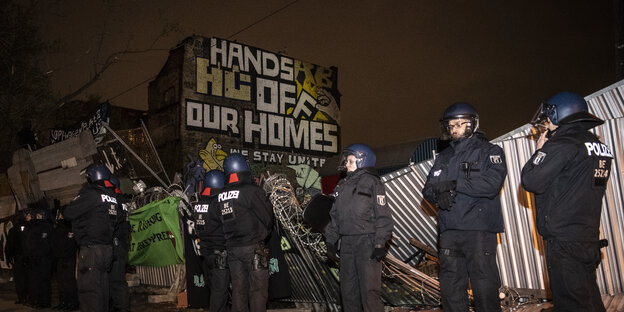 Polizeibeamte stehen auf der Straße vor dem früheren "Köpi"-Wagenplatz an der Köpenicker Straße. Im Hintergrund ist das markante Wand-Graffiti auf der Außenwand der Köpi zu lesen: "Hands off our home!".