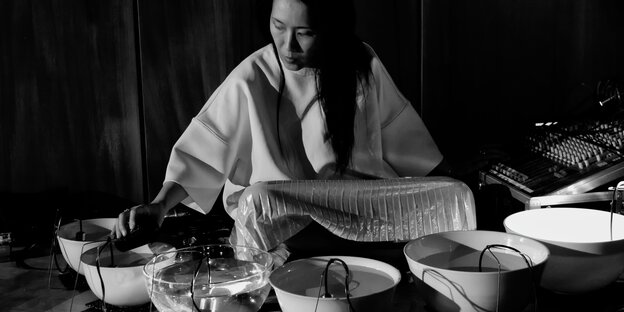 Die Künstlerin Tomoko Sauvage im Schneidersitz, um sie herum mit Wasser gefüllte Schalen, darin Mikrofone