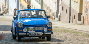 Das Foto zeigt den DDR-Radsportler Schur als Beifahrer in einem blauen Trabant-Cabrio.