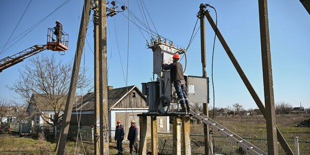 Elektriker reparieren Stromleitungen an Hochspannungsmasten in ländlicher Umgebung