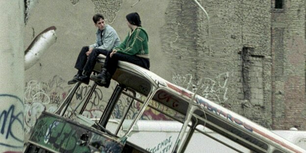 Zwei Personen sitzen auf einem zerstörten Bus im Berlin der Neunzigerjahre