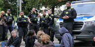 Eine Gruppe Polizist*innen steht vor auf dem Boden sitzenden Protestierenden
