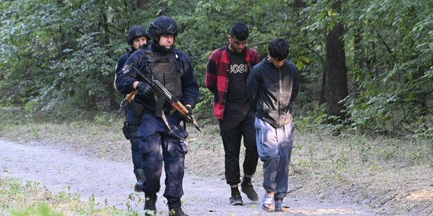 Bewaffnete Polizisten mit zwei Zivilisten im Wald.