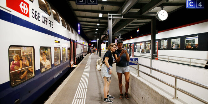 Zwei Züge und Personen in einem Bahnhof.