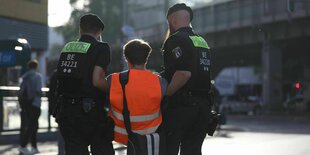 Zwei Polizisten tragen einen Aktivisten der letzten Generation in Warnweste von der Straße