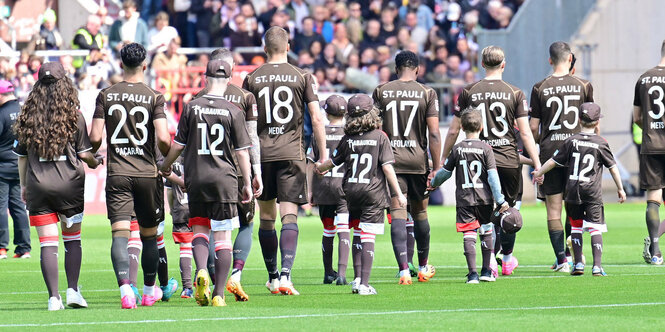 Fußballspieler gehen auf das Speilfeld, mit Nachwuchsspieler:innen an der Hand.