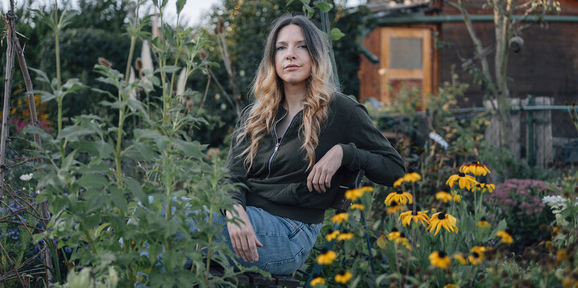 Portrait Marlen Hobrack sitzend zwischen Pflanzen, im Hintergrund ein Schuppen