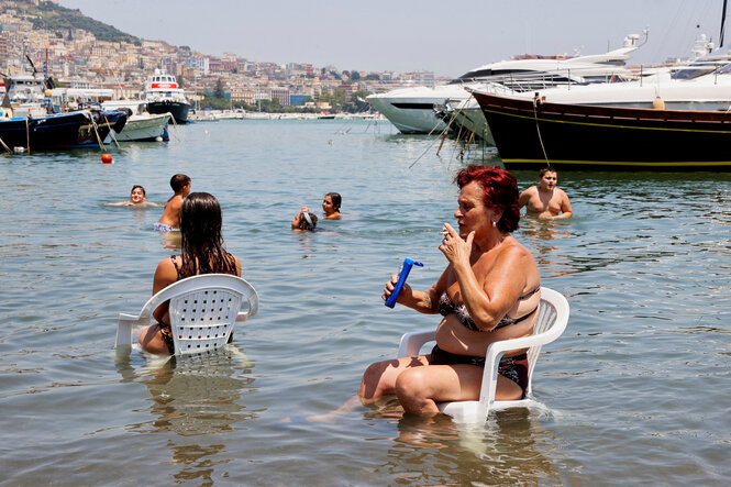 Menschen sitzen im Wasser, eine Person raucht.