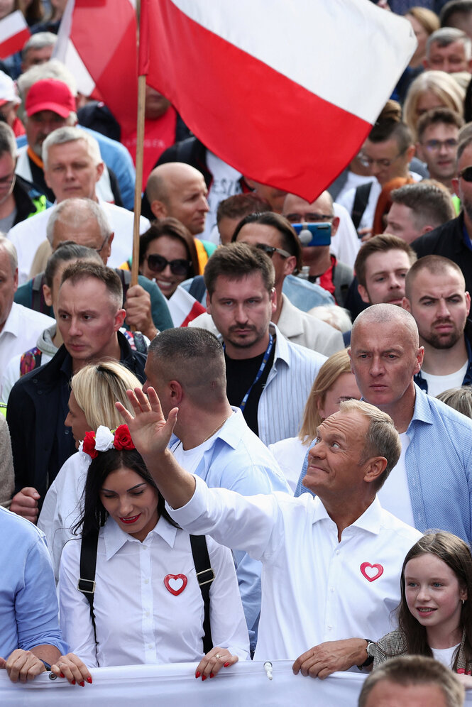 Polnische Flaggen, Menschen auf einer Kundgebung stehen eng gedrängt, Donald Tusk winkt