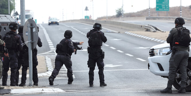 Soldaten blockieren eine Schnellstraße, einer gebietet einem herankommenden Fahrzeug Halt