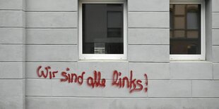 Wir sind alle links! Graffiti in roter Farbe an einer hellen Hauswand