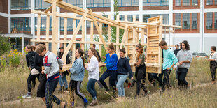 Menschen tragen eine Holzkonstruktion.