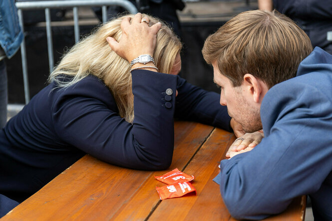 Nancy Faeser beugt sich über einen Tisch und stützt ihren Kopf in die Hände, Kevin Kühnert sitzt ihr gegenüber und spricht mit ihr