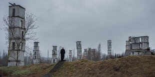 Turmähnliche Skulpturen stehen in einer Landschaft, Anselm Kiefer wandelt dazwischen