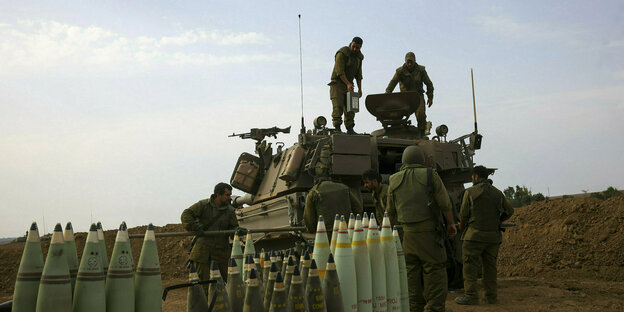 Israelische Soldaten stehen vor und auf einem Panzer, vor dem Munition in Reihen aufgestellt wurde