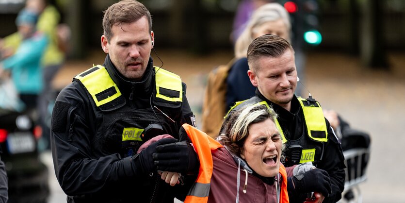 Eine Aktivistin wird von zwei Polizisten mit verdrehten Handgelenken abgeführt