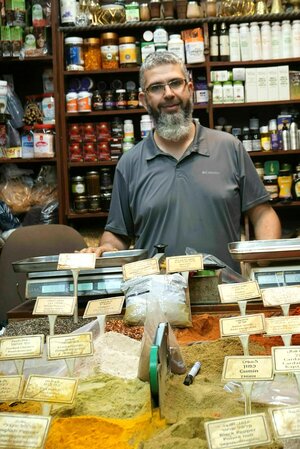 Ein Gewürzhändler steht in seinem Geschäft in der Altstadt. Eine große Auswahl an offenen Gewürzen liegt vor ihm