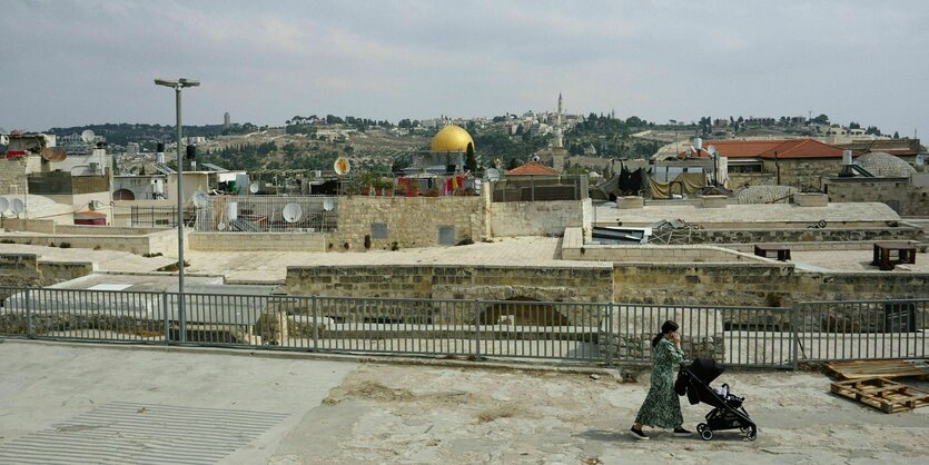 Eine Frau unterwegs mit d em Kinderwagen in der Altstadt von Jerusalem, im Hintergrund ist der Felsendom zu sehen