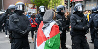 Eine Person mit Palästinaflagge steht vor mehreren Polizisten