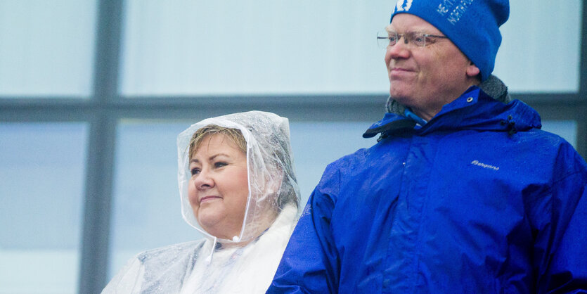 Erna Solber trägt ein Regencape, an dem Tropfen herunterrinnen, Sindre Finnes trägt eine blaue Mütze und eine blaue Jacke