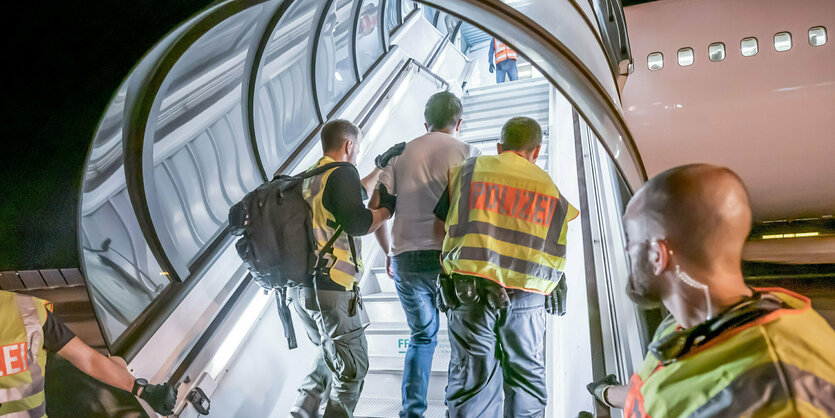 Eine Person wird von Polizisten in ein Flugzeug geführt.