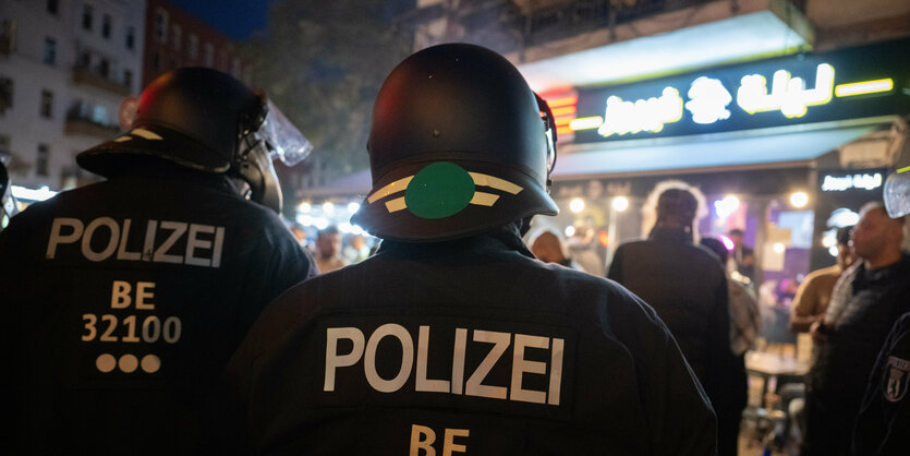 Behelmte PolizistInnen von hinten vor einem Imbiss