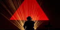 Die Künstlerin ist nur als Schattenriss zu sehen, umgeben von einem Lichterkranz. Im Hintergrund ein leuchtendes rotes Dreieck.