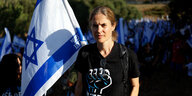 Portrait von Shikma Bressler. Sie steht neben einer Israelfahne, auf ihrem T-shirt ist eine gereckte Faust zu sehen