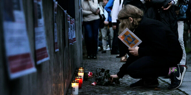 Ein Kind kniet vor dem Zaun der Synagoge am Fraenkelufer und legt Rosen nieder